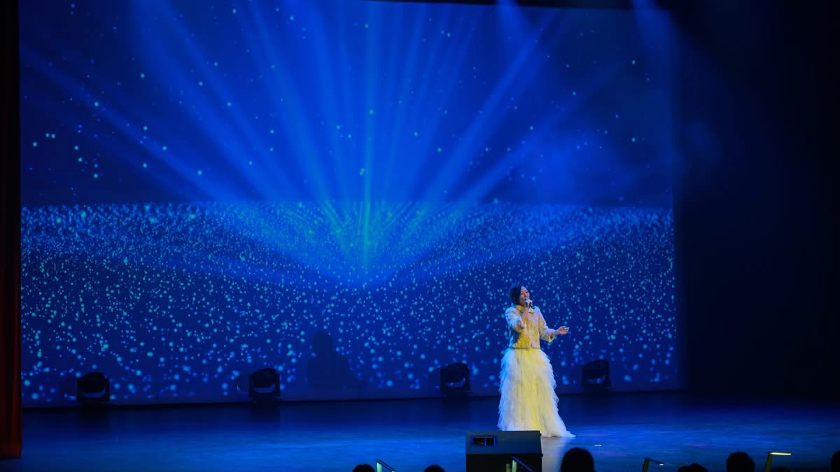 Anita Tong en prestation sur une scène de concert sous une projection étoilée