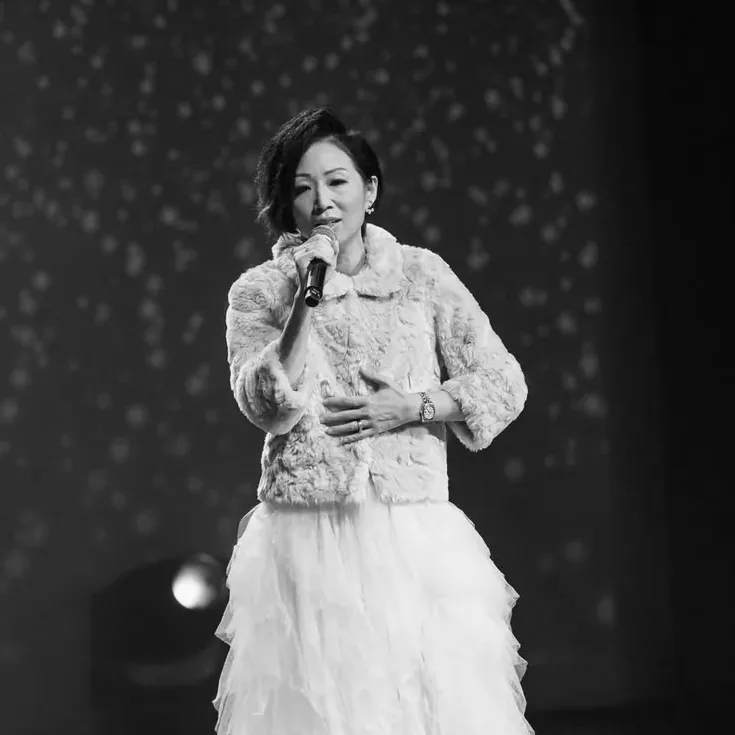 Anita Tong chantant en veste de fourrure et jupe de tulle devant un fond étoilé