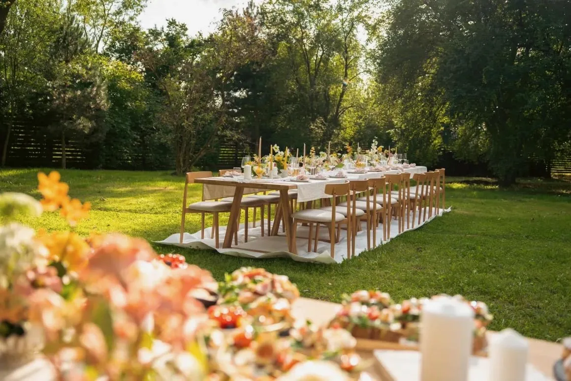 Long wedding table set on a sunlit lawn at golden hour, framed by summer flowers